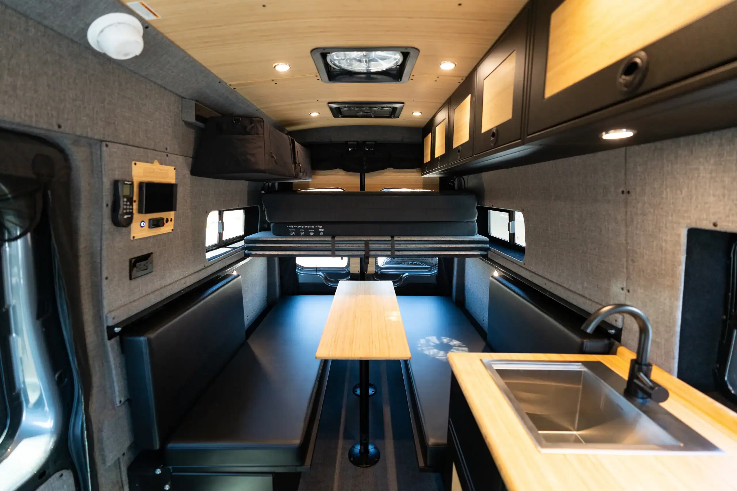 Modern van interior with seating, table, and kitchenette for travel and camping.