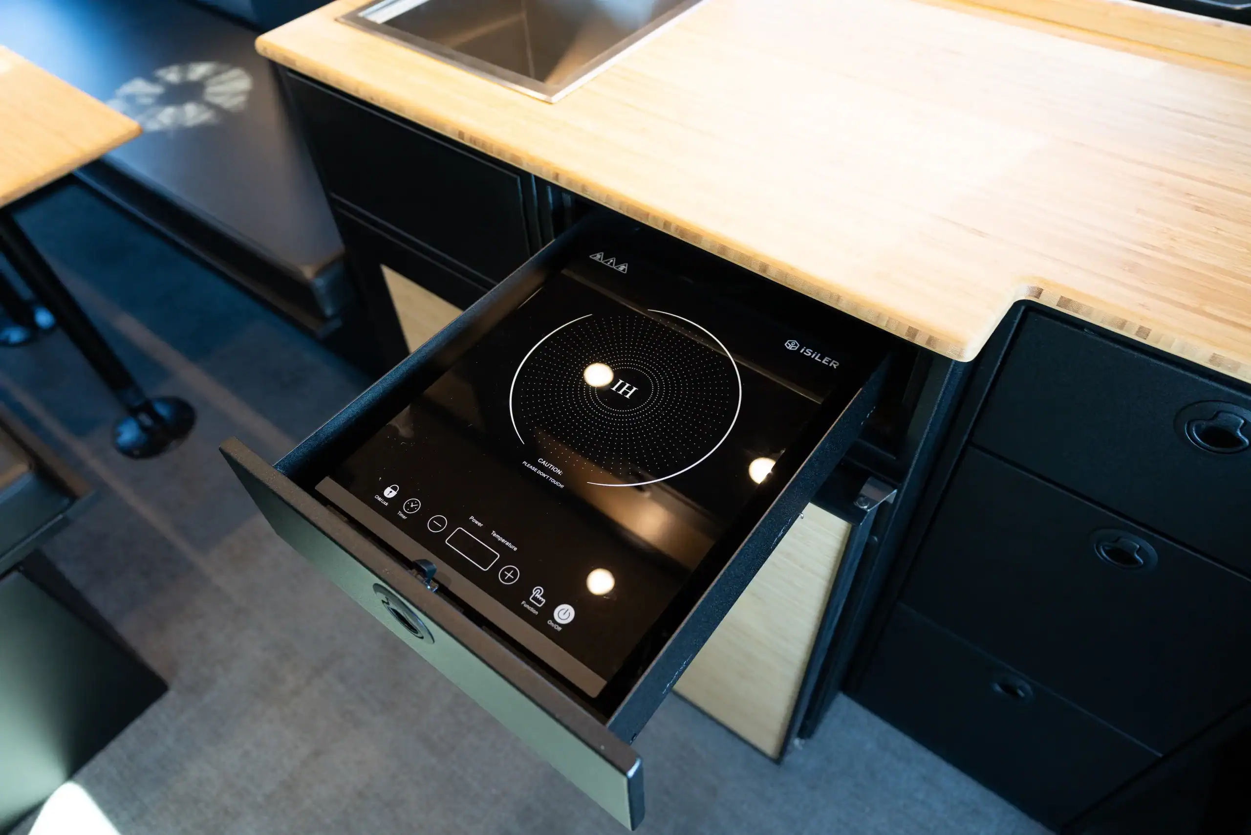 Built-in induction cooktop in a van conversion kitchen by Vanworks.