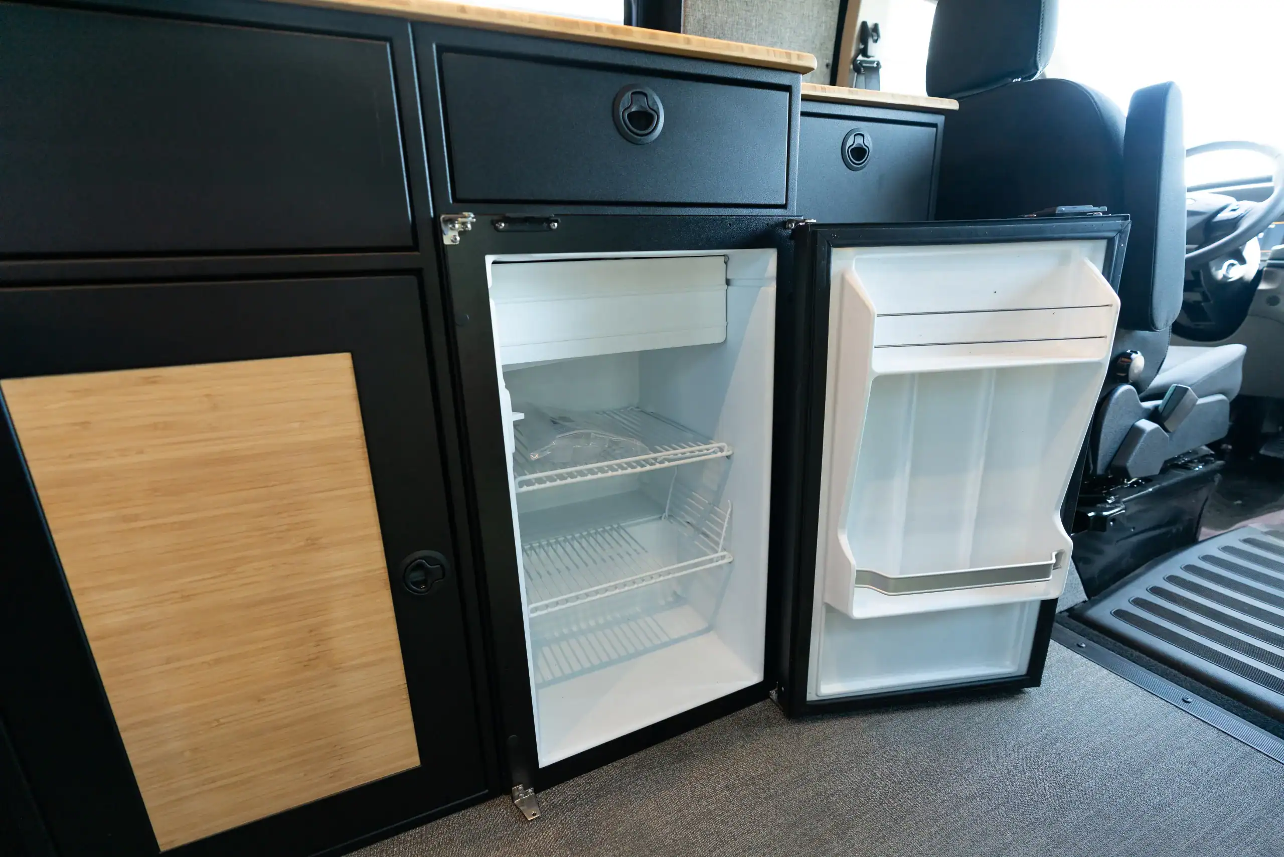 Compact mini fridge and storage cabinet in van interior.